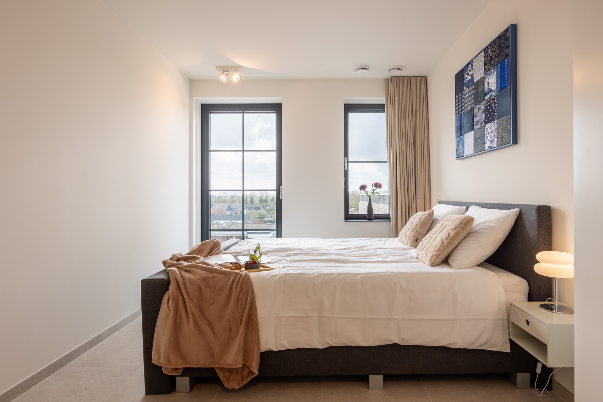 Lichte slaapkamer met tweepersoonsbed, uitzicht op Cadzand-Bad en Delfts blauw patchwork kunstwerk aan de muur