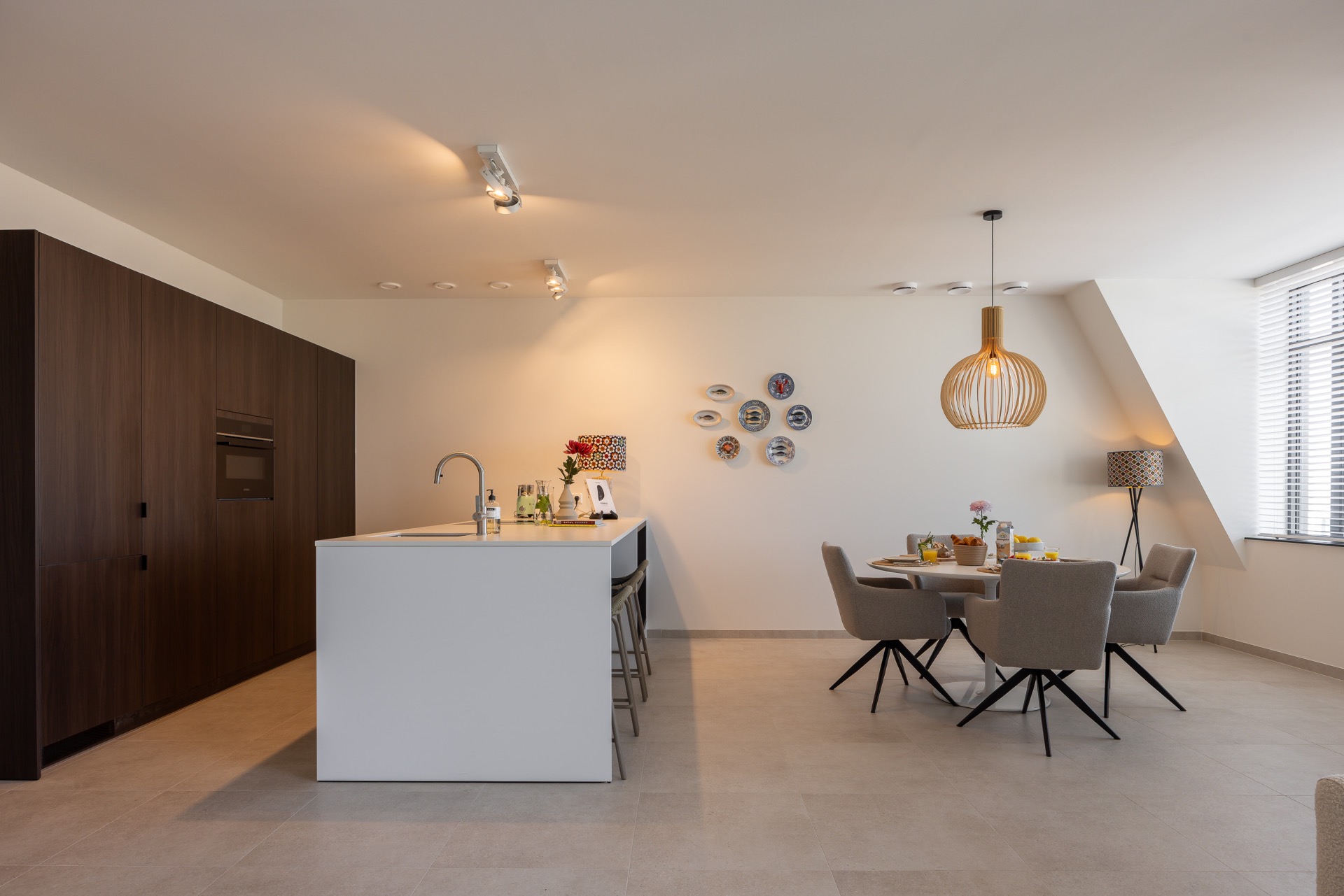 kookeiland, donkere kastenwand en ronde eettafel met grijze stoelen in appartement Cadzand-Bad